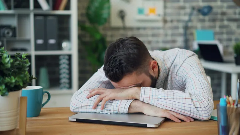 Homme épuisé, la tête posée sur ses bras repliés sur son ordinateur portable