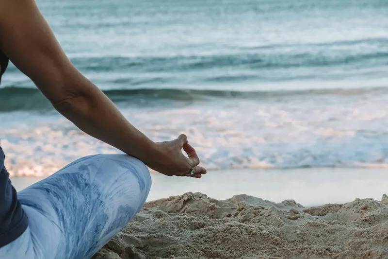 Personne assise en méditation sur le sable, face à la mer au petit matin